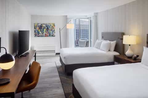 Modern hotel room with two queen beds, work desk, flat-screen TV, and floor-to-ceiling windows with city views