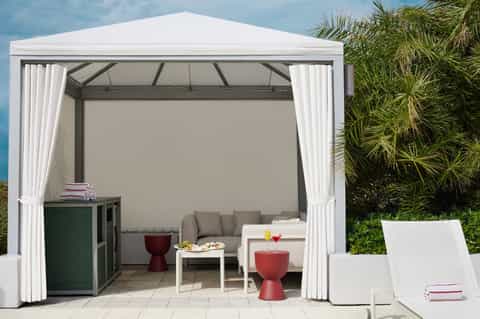 Modern white gazebo with curtains, lounge seating, and tropical plants in resort setting