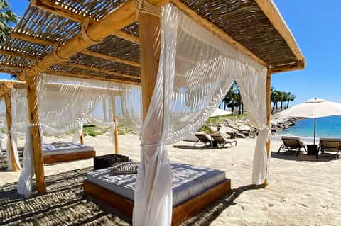 Beachfront cabanas with white curtains and wooden pergolas overlooking the ocean and sand