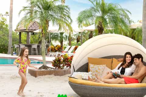 Beachside resort with family enjoying sand area, palm trees, pool, and modern cabana seating