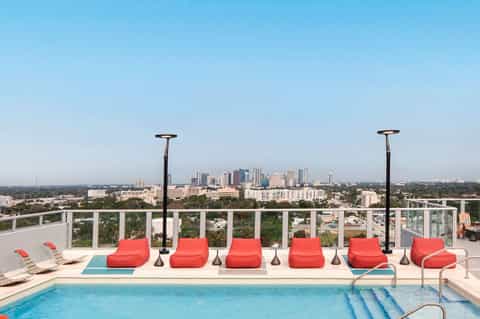 Rooftop pool area with red loungers, heaters, and city skyline view in the distance