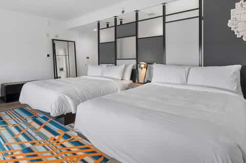 Contemporary hotel room with two queen beds, dark headboard, geometric patterned floor rug, and minimalist design
