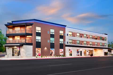 Contemporary mixed-use building with red brick, white base, glass storefronts, and blue roofline at dusk