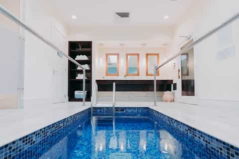 Indoor lap pool with blue tile flooring, white walls, mirrors, and wooden lockers in spa facility