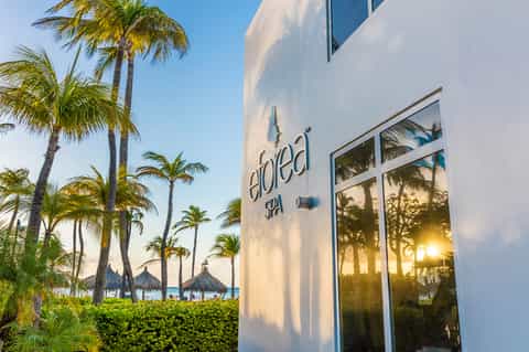 Eloed Spa exterior with white modern architecture, palm trees, and ocean view at sunset