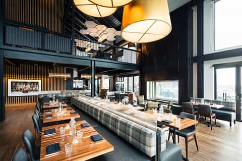 Contemporary restaurant with high ceilings, pendant lighting, and large windows overlooking city