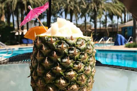 Tropical cocktail in pineapple with decorative umbrellas by resort pool and palm trees