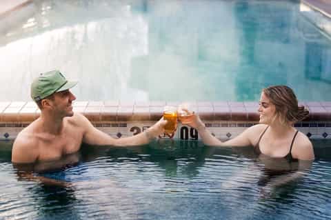Couple toasting with drinks in a hot spring pool with tiled edge