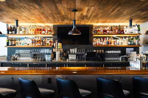 Upscale bar with wooden ceiling, extensive liquor shelves, black pendant light, and blue bar stools