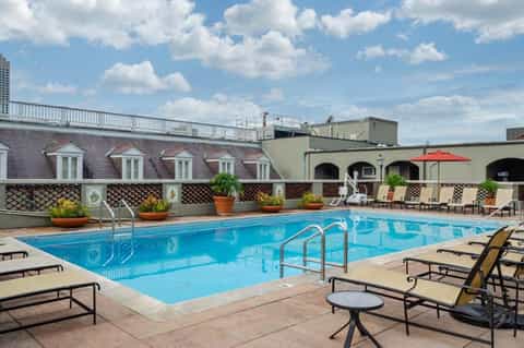 Rooftop outdoor pool with lounge chairs, decorative lattice fence, and mansard-roof building beyond