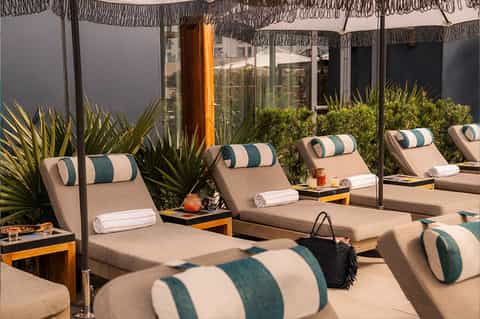 Upscale pool lounge with striped cushioned chairs under fringed umbrellas and tropical plants