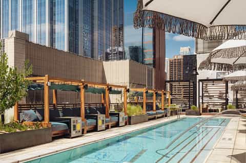 Rooftop pool deck with wooden cabanas, white umbrellas, city skyline views, and lounging areas