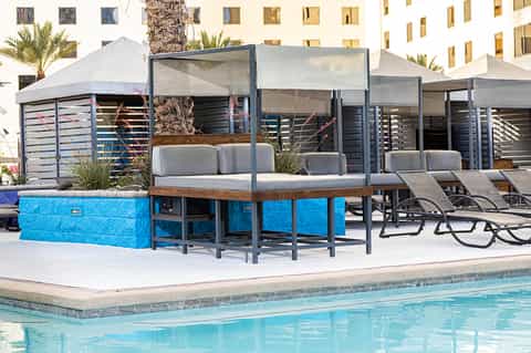 Poolside cabanas with blue accents and gray lounge seating under white tent canopies