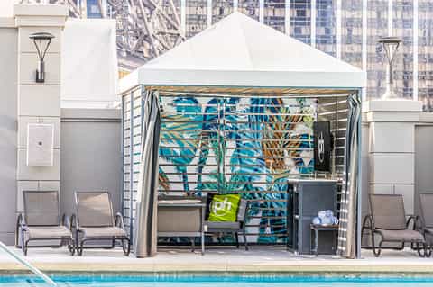 Poolside cabana with white tent canopy, striped curtains, tropical plant backdrop, and lounge chairs
