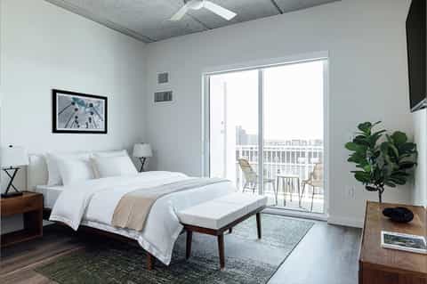 Bright hotel bedroom with sliding glass doors opening to balcony overlooking cityscape