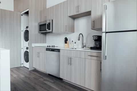 Modern kitchen with gray wood cabinetry, stainless steel appliances, and stacked washer/dryer units