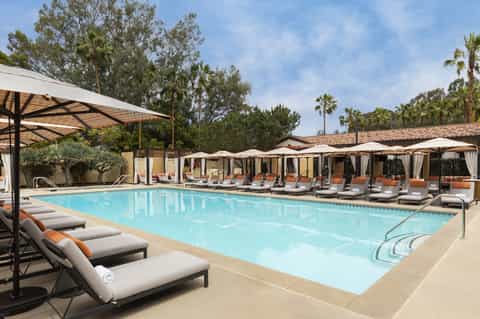 Resort pool with turquoise water, lounge chairs, umbrellas, and palm trees under blue sky