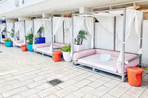 Modern outdoor lounge area with white canopy daybeds, pink cushions, and colorful accent seating