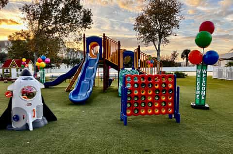 Outdoor children's playground with colorful slides, climbing structures, and balloons on manicured lawn