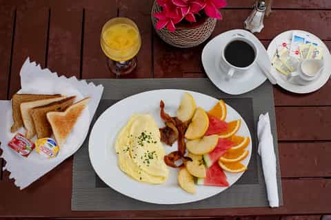 Breakfast plate with omelet, bacon, fresh fruit, and toast with orange juice and coffee