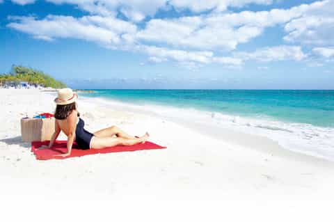 Woman relaxing on red towel at pristine beach with turquoise ocean and white sand