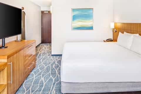 Modern hotel room with queen bed, wooden dresser, flat-screen TV, and ocean-themed artwork