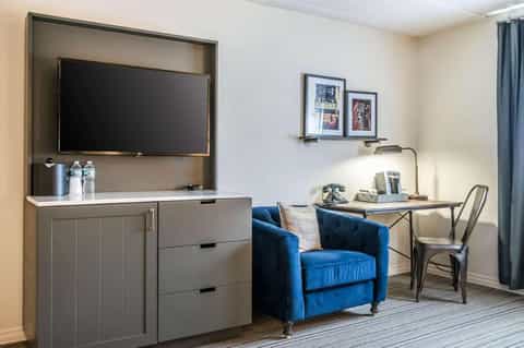Modern hotel room with wall-mounted TV, blue armchair, desk workspace, and contemporary furniture
