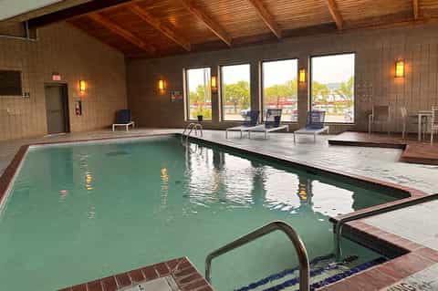 Indoor swimming pool with green water, lounge chairs, wooden beam ceiling, and large windows