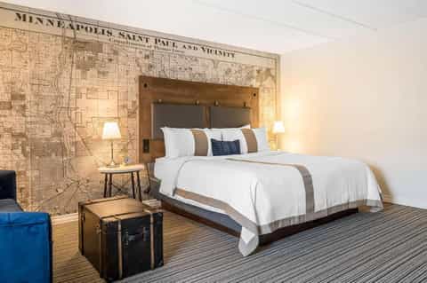 Hotel bedroom with wooden headboard featuring Minneapolis map, white bedding, and vintage suitcase