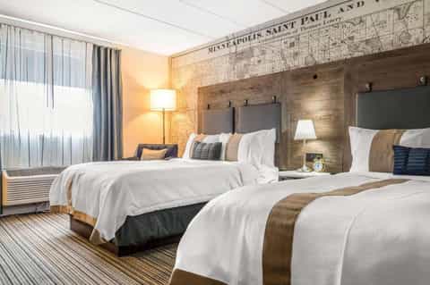 Modern hotel room with two queen beds, wood headboards, and vintage map wall décor in warm lighting