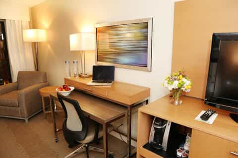 Hotel room workspace with wooden desk, laptop, lamp, and flowers beside TV