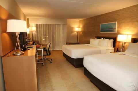 Hotel room with two queen beds, work desk, warm lighting, and patterned wallpaper