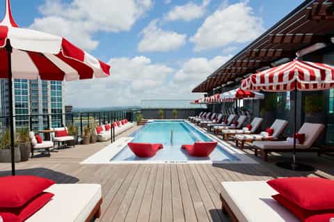 Rooftop pool deck with red and white striped umbrellas, loungers, and city skyline views