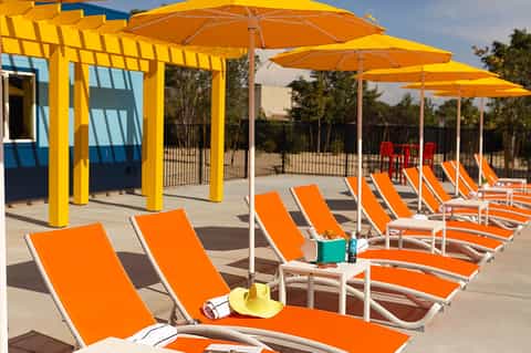 Rows of orange lounge chairs under yellow umbrellas and pergolas on a sunny patio