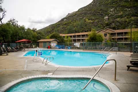 Resort outdoor pool complex surrounded by lounge chairs with mountain backdrop and hotel buildings