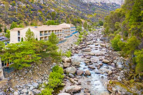 Riverside hotel nestled in mountain valley with rocky stream and forested landscape