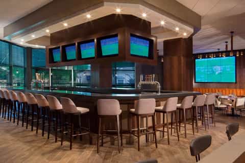 Modern sports bar with multiple screens, dark wood bar counter, and upholstered seating with ocean views