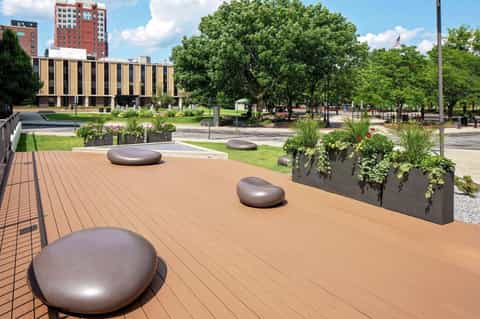 Urban rooftop terrace with metallic seating pods, planter boxes, and city park views