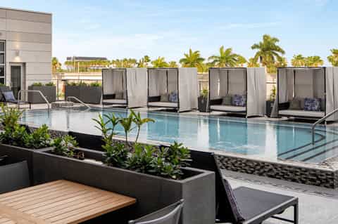 Rooftop pool deck with cabanas, lounge chairs, palm trees, and city skyline views