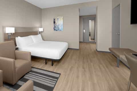 Contemporary hotel bedroom with queen bed, wood flooring, neutral tones, and ensuite bathroom