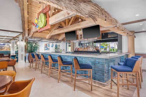 Modern tropical bar with thatched ceiling, blue stone bar counter, wooden beams, and orange leather seating