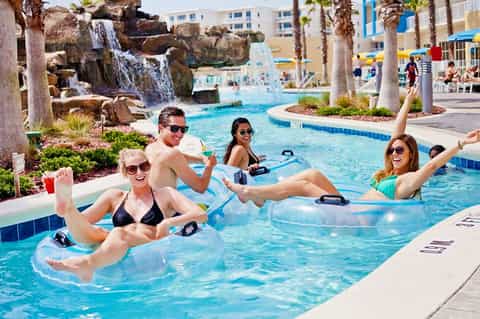 Resort guests relaxing in clear blue lazy river with waterfall and palm trees