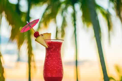 Tropical cocktail with pineapple, cherry, and pink umbrella garnish against palm fronds backdrop
