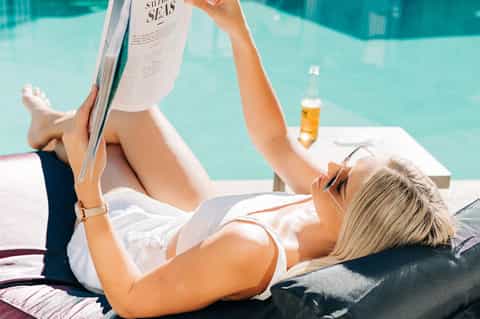 Woman relaxing poolside reading magazine with turquoise water and beer bottle nearby