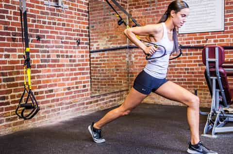 Fit woman performing suspension training exercise with TRX straps in brick-walled gym