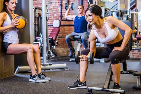 Women exercising with dumbbells and weights in a modern gym with brick walls