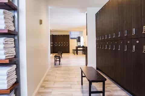 Spa locker room with dark wooden lockers, folded towels on shelves, and wooden benches in hallway