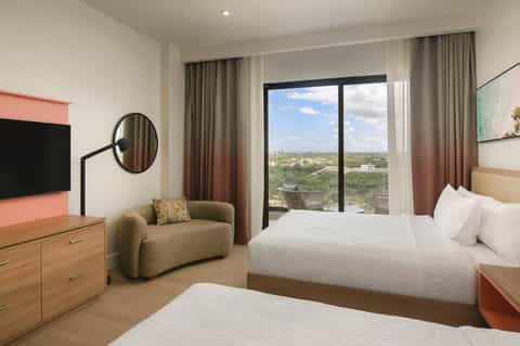 Spacious hotel room with two beds, city views from floor-to-ceiling windows, and modern furnishings