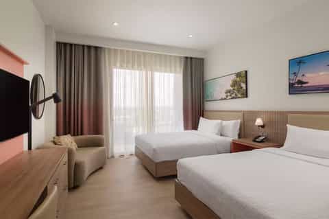 Modern hotel room with two beds, beige headboard, coral accents, and balcony access with city views