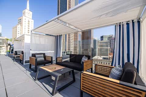 Urban rooftop lounge with modern furniture, retractable shade canopy, and city skyline views